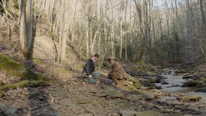 Two soldiers with rifles take cover in the woods