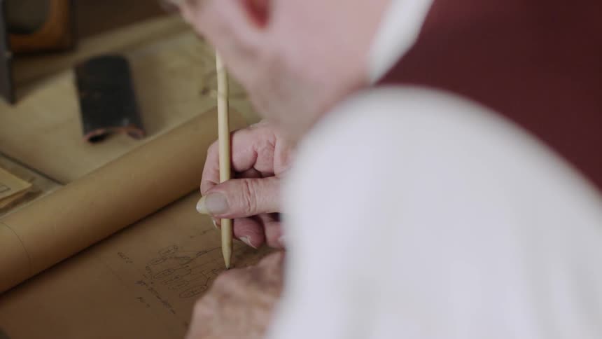 A man is using a magnifying glass to exam papers on a desk in daylight