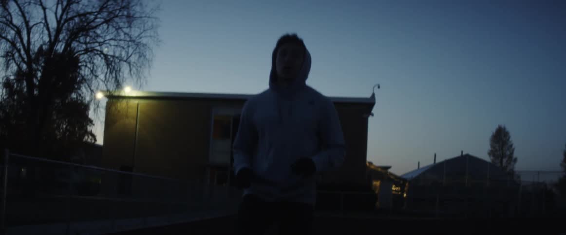 A man in a sweatshirt jogs in place outside of a building at night