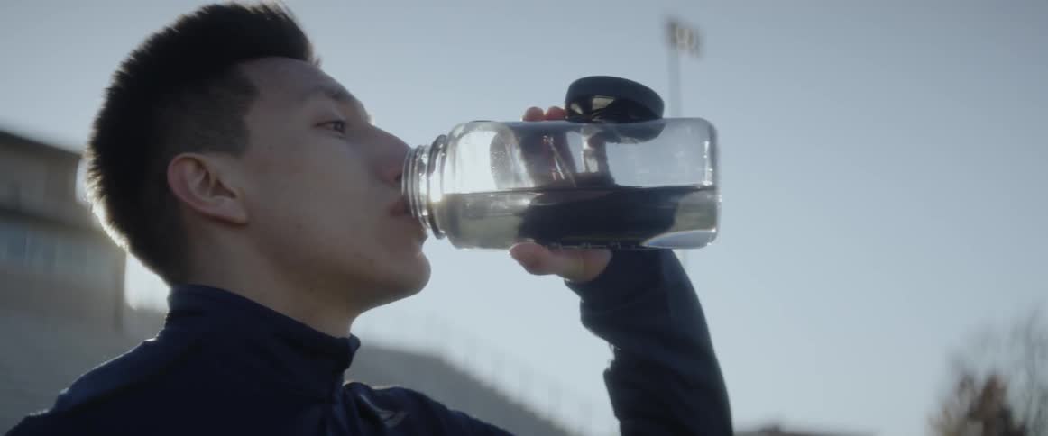 An athlete is taking a drink of water as he pauses working out on cold day