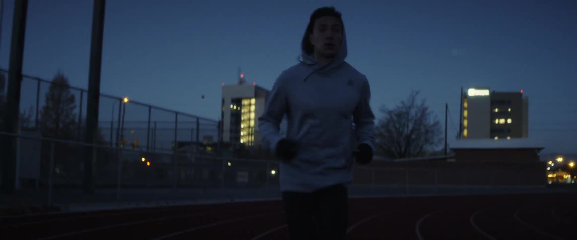 A man with his hood up runs around a track at night