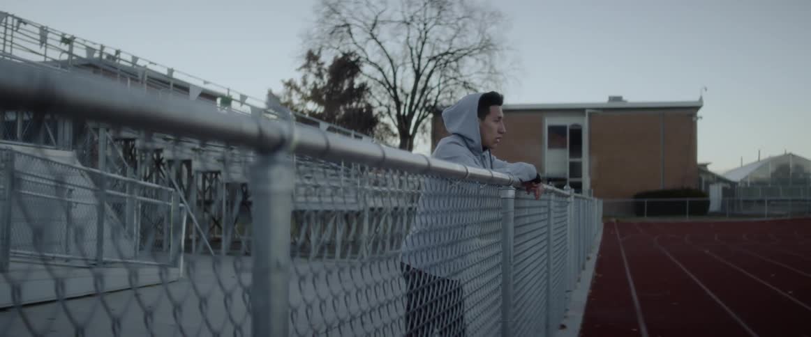 A male athlete is breathing heavy as he leans against a fence at dawn