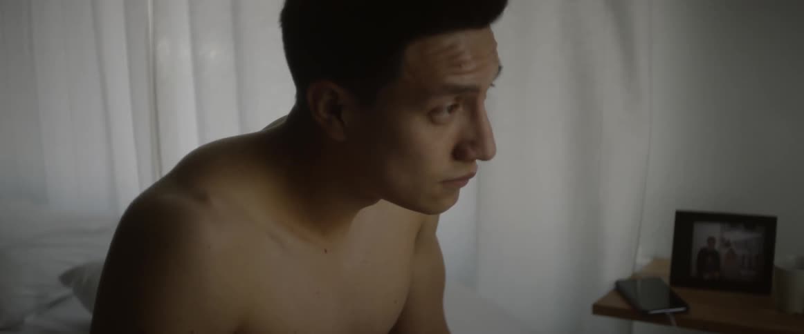 Man sitting on bed rubs his head then looks towards picture frame