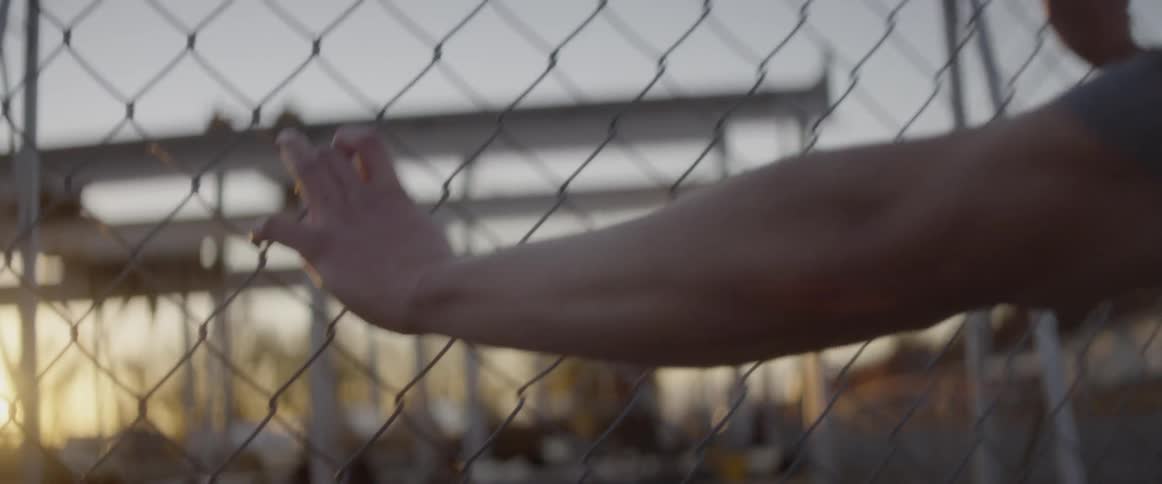 Man leans against a chain link fence at sunset