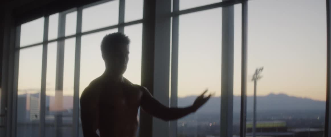 A man practices dance poses and moves near floor to ceiling windows