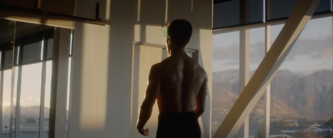 A shirtless man stands indoors