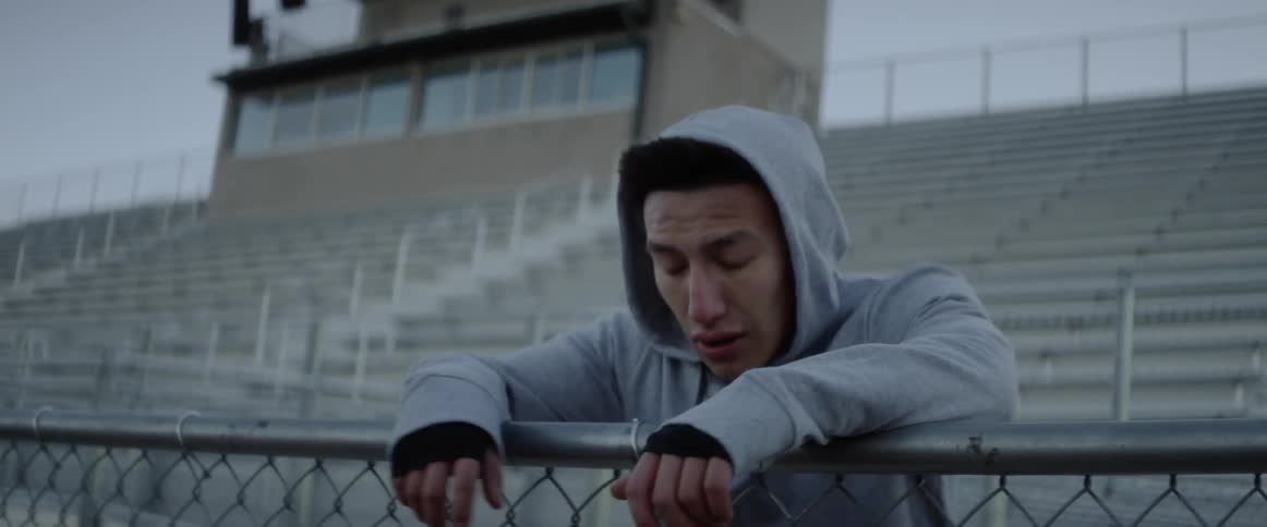 A man rests and exhales while leaning on a chain link fence