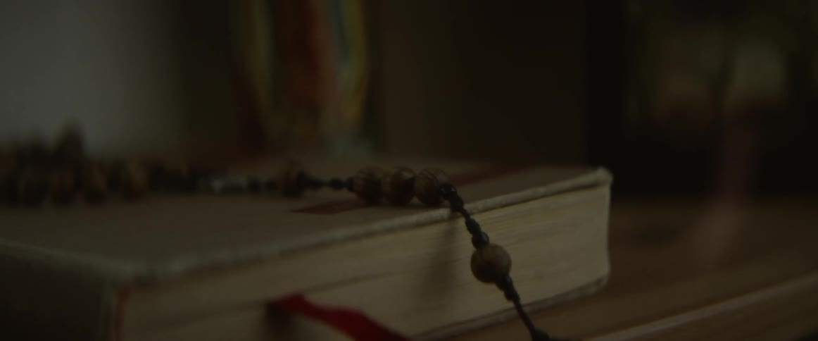 A bible with a rosary on top sits on a shelf next to a candle