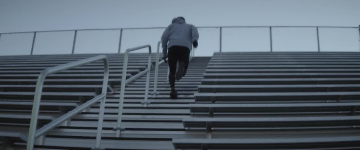 A male athlete is jogging up the stairs on a set of bleachers on a cloudy morning