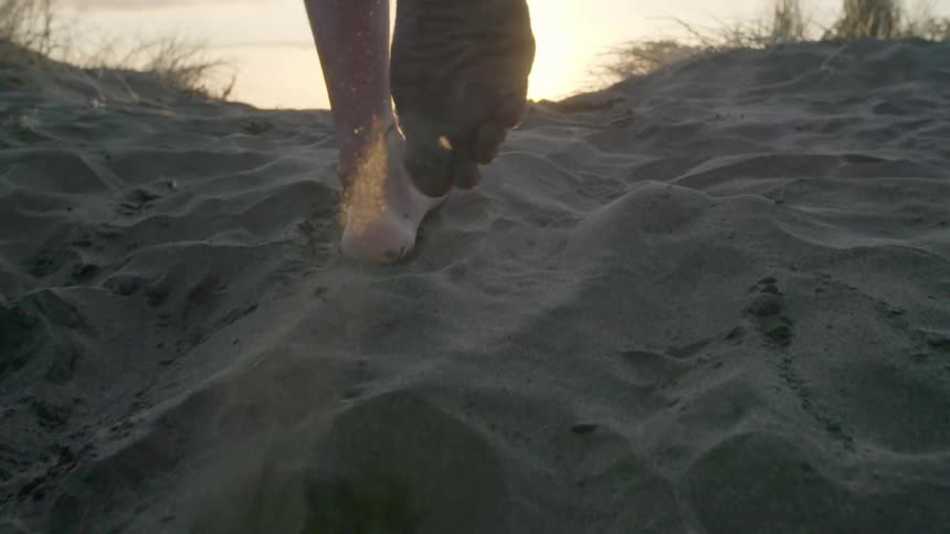 Feet walking in the sand towards a rising sun