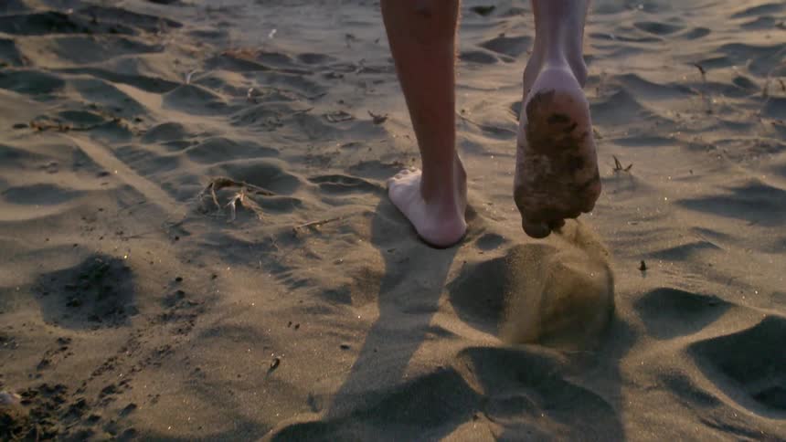 Tight shot of a man's feet and calves as he walks through sand