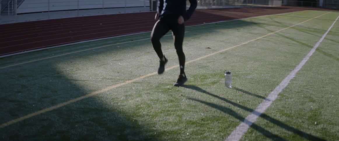 A man is jogging in place on the field near his water bottle