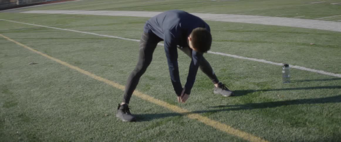 Man leans over and stretches while standing on a sports track