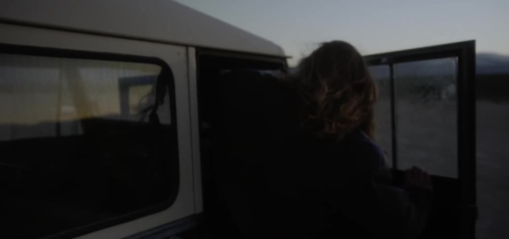 Man climbs into a vehicle parked in a rural field at dusk