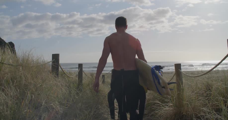 A man and woman walk towards the beach holding surfboards