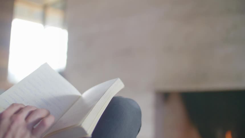 A woman reads a book by the fire