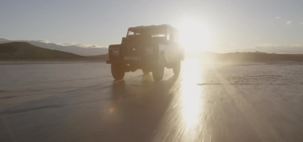 A vehicle drives across a rural field at sunset