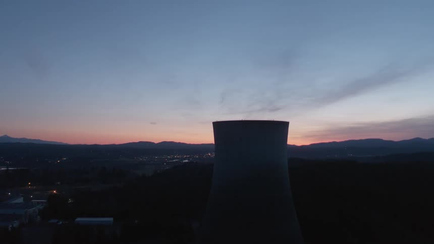Pullback reveal of a cooling tower and nuclear power facility at dusk