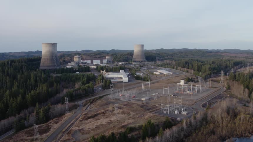 Flying over an electrical substation and power lines with a nuclear plant in the distance