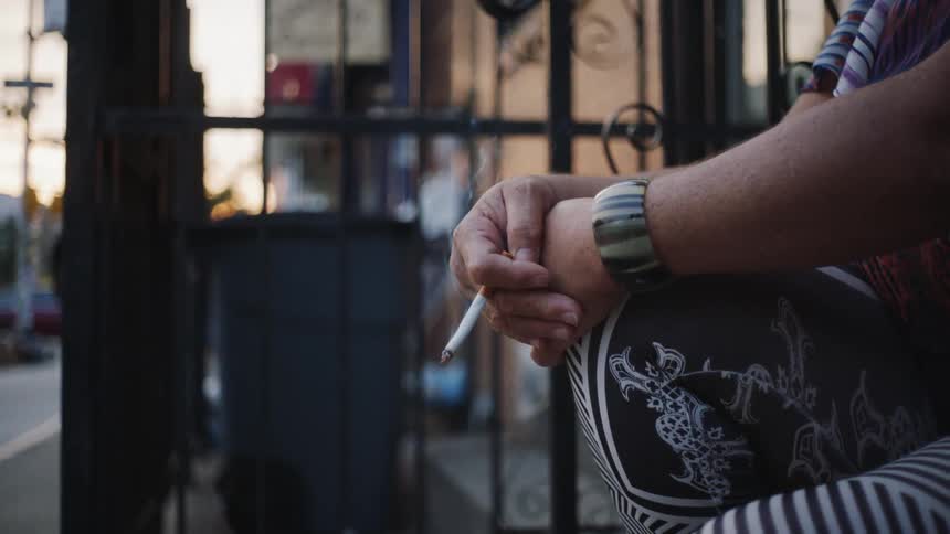 A woman sitting on a stoop holds a lit cigarette
