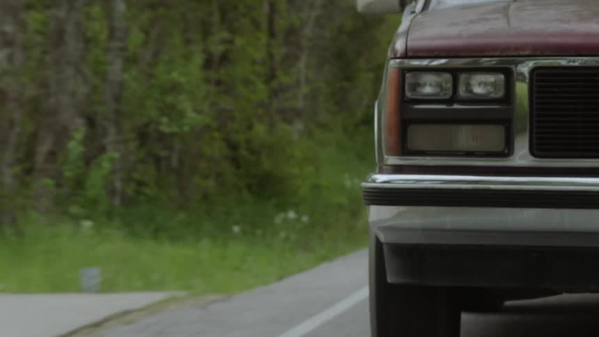 The vehicle moves down the road near the green trees