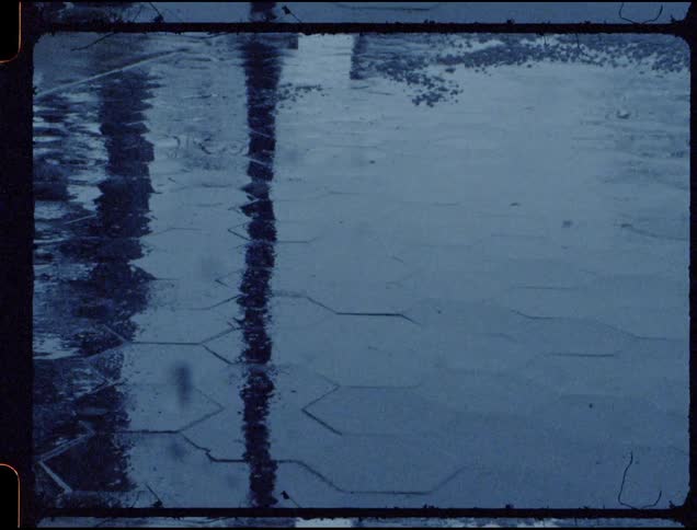 Rain hits a street and the puddle reflects some surroundings