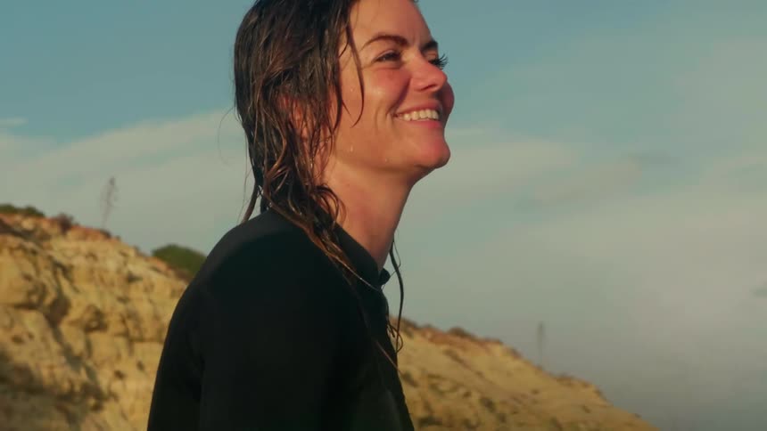 A woman in a wetsuit with wet hair smiling