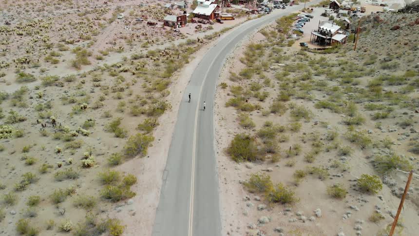 Two skateboarders ride on a rural road