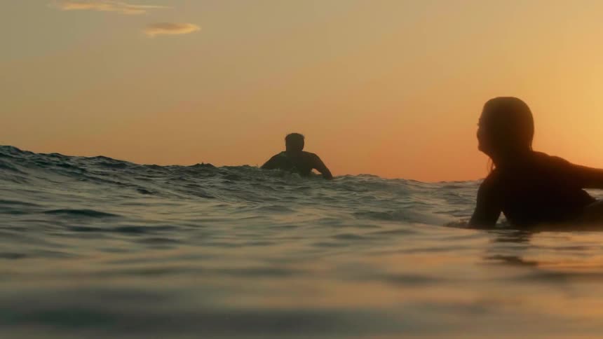 Surfers swim in the ocean at sunset