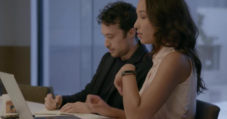 A man and woman are sitting at a conference table working in daylight