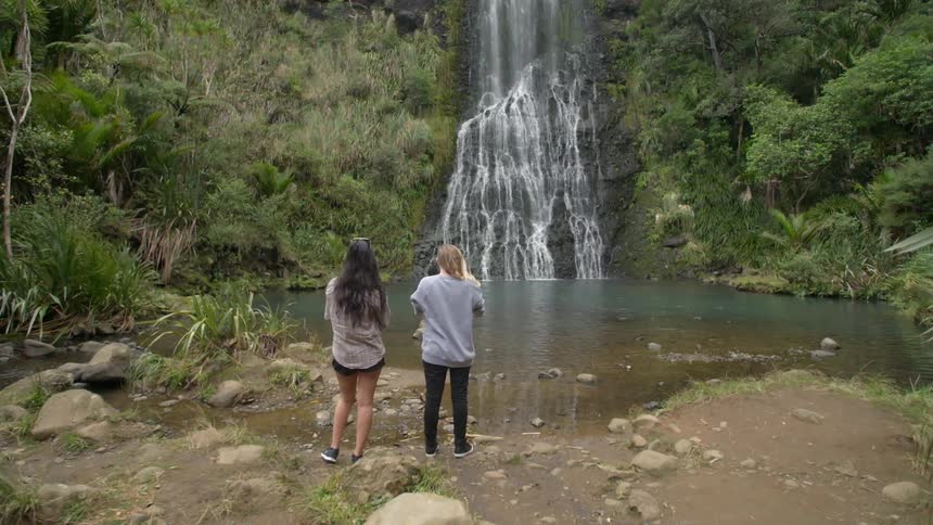Two women standing on a bank watching a waterfall