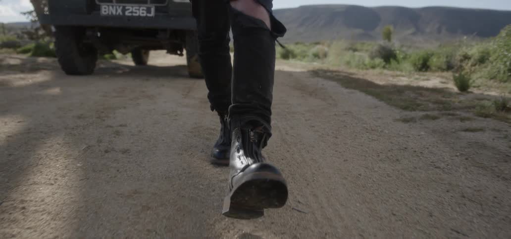 A man with ripped jeans walks in a desert