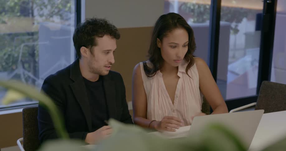 A man and woman are sitting at a conference table working in daylight