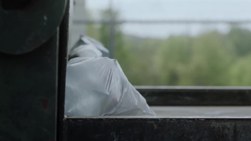 A bag of trash is being compacted into a machine in daylight
