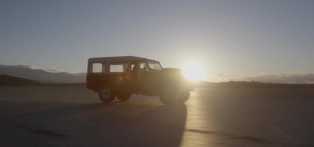 Vehicle drives across rural dirt field at sunset