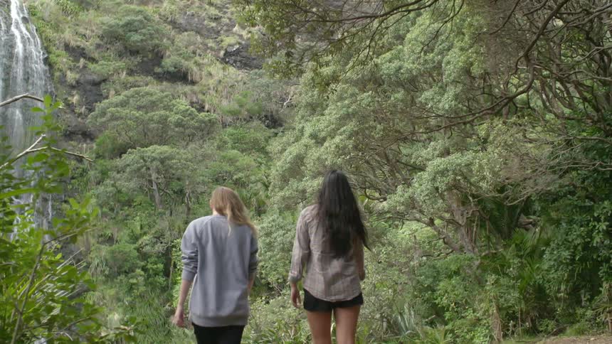 Two women hike through the woods towards a waterfall