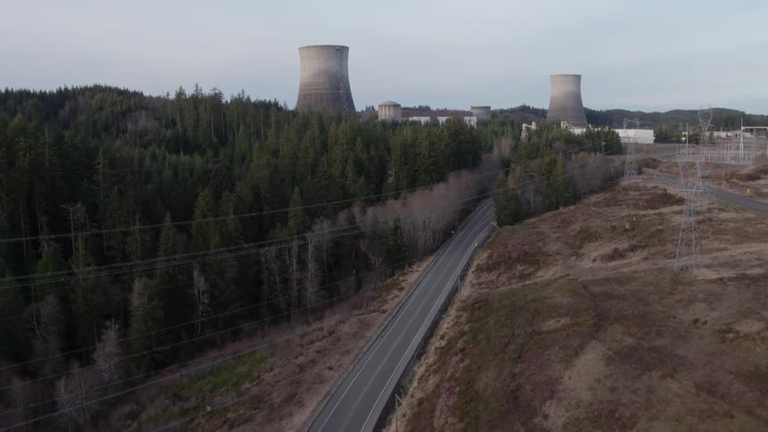 Flying up from a roadway to reveal a nuclear power station through the trees