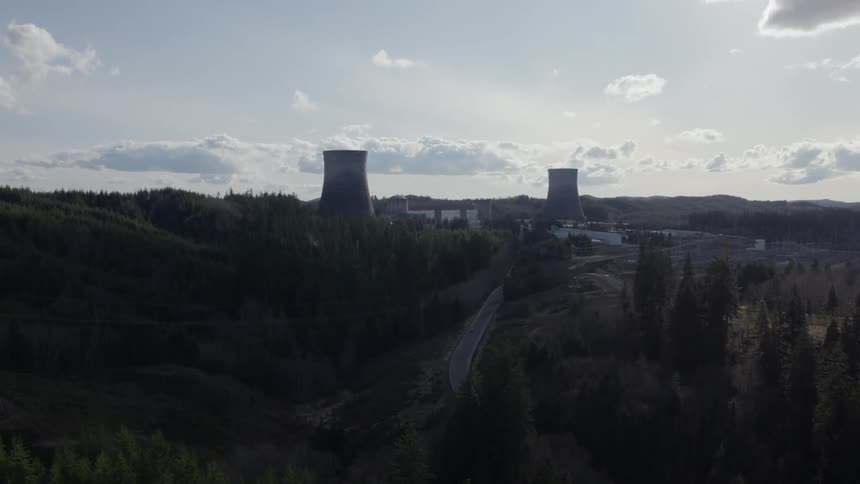 Ascending along a wooded hillside to show a power generating station in the distance