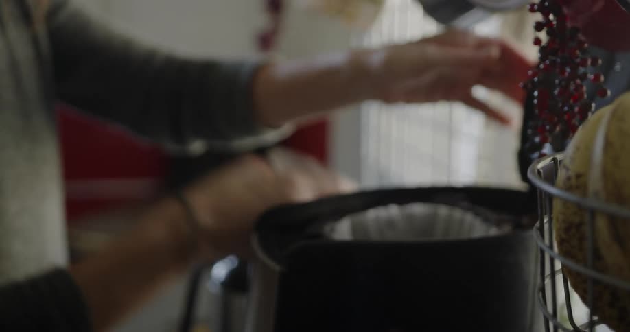 A woman pours coffee grounds into a coffee machine