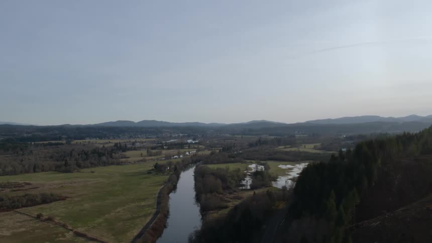 A river flows through farmland next to mountain foothills