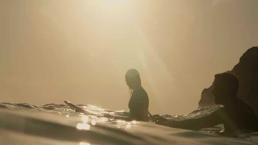 Surfers float in the ocean at sunset