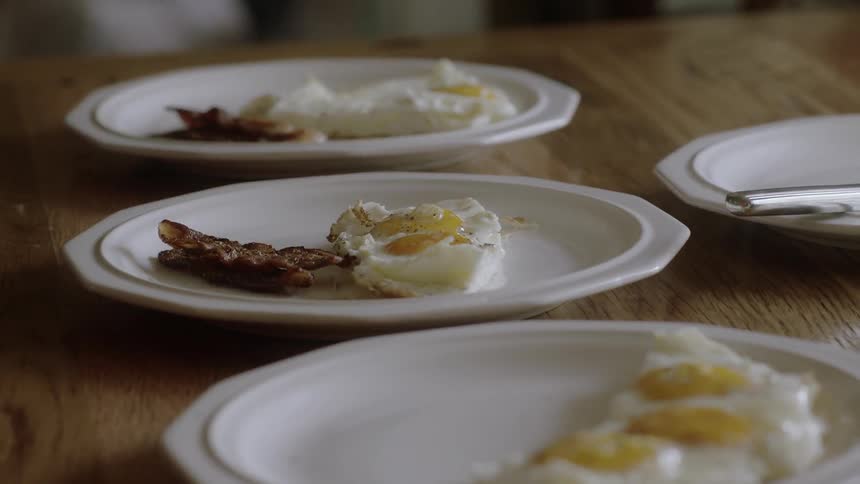 Plates on the table are being filled with bacon and eggs