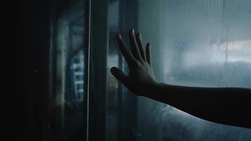 A person touches the glass of a door at night