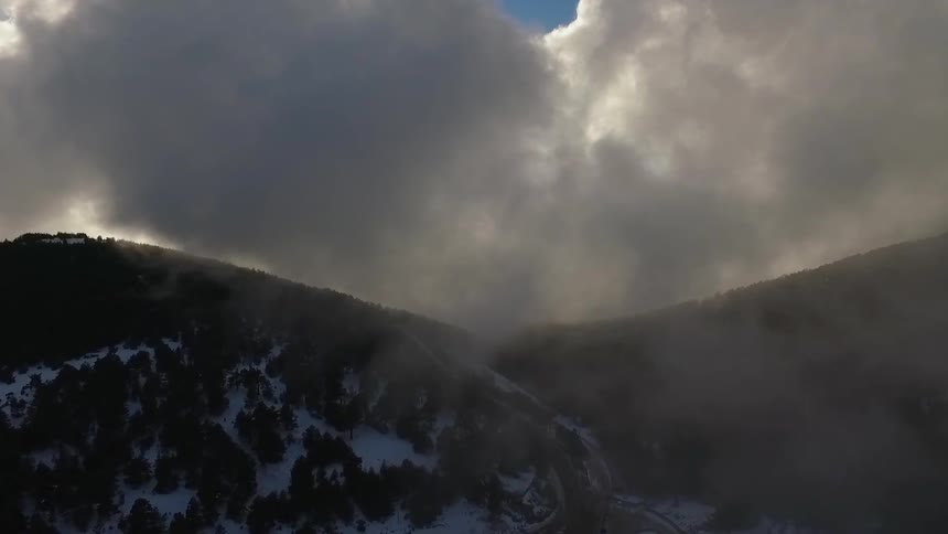 Fog and clouds hang over snow and tree covered slopes