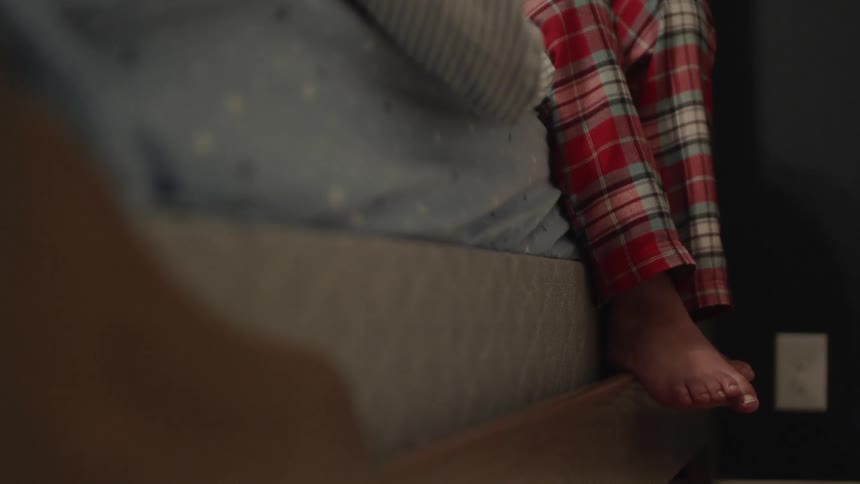 A child is sitting with their feet dangling over the edge of their bed