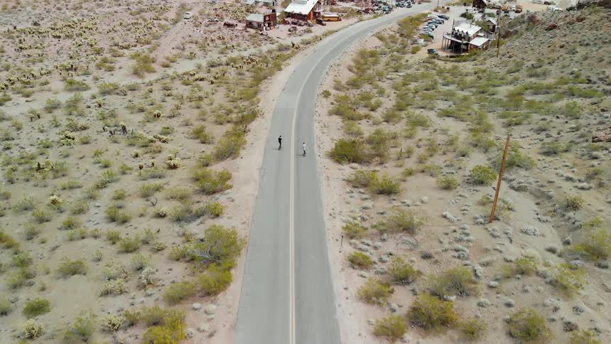 Skateboarders ride on a rural road