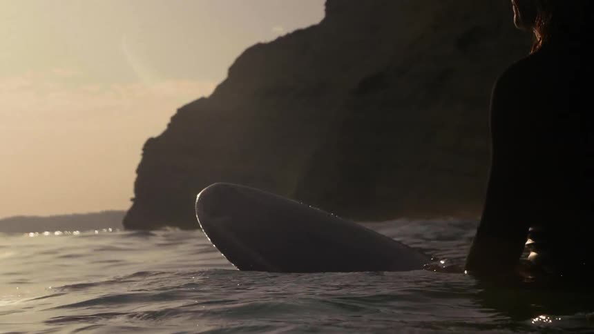 A surfer sits on his board in the ocean at sunset