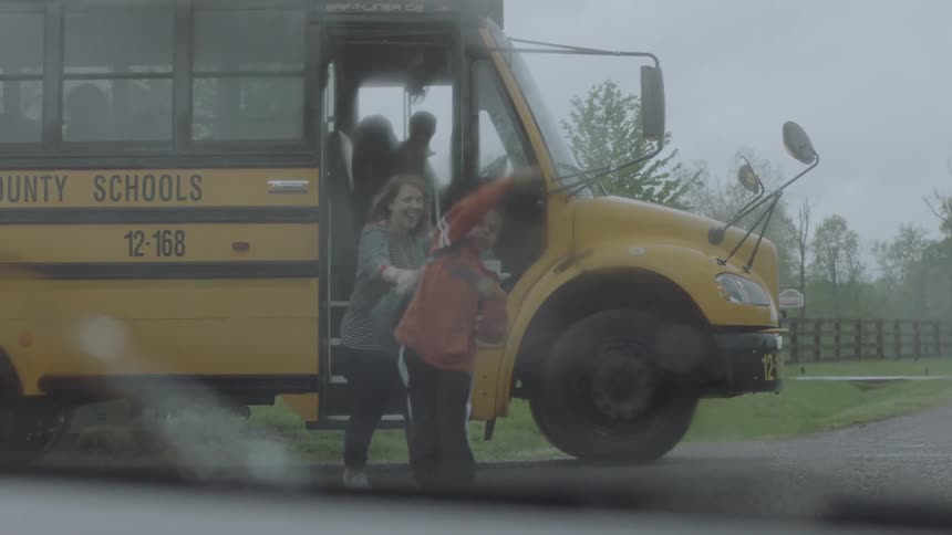 A woman greets a boy getting off a school bus