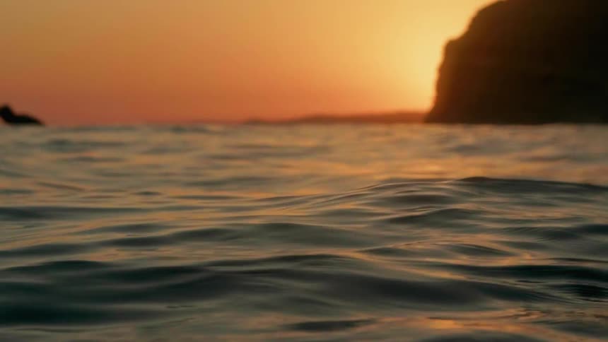 A surfer swims in the ocean at sunset