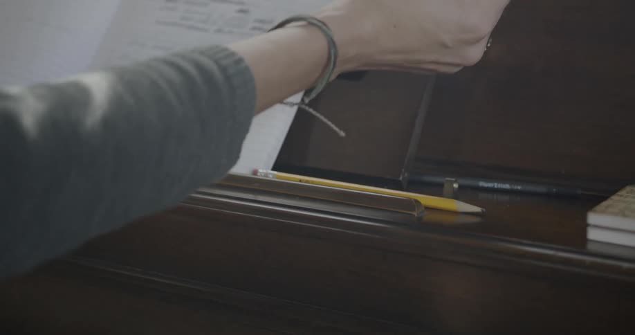 A woman opens a notebook on top of a piano